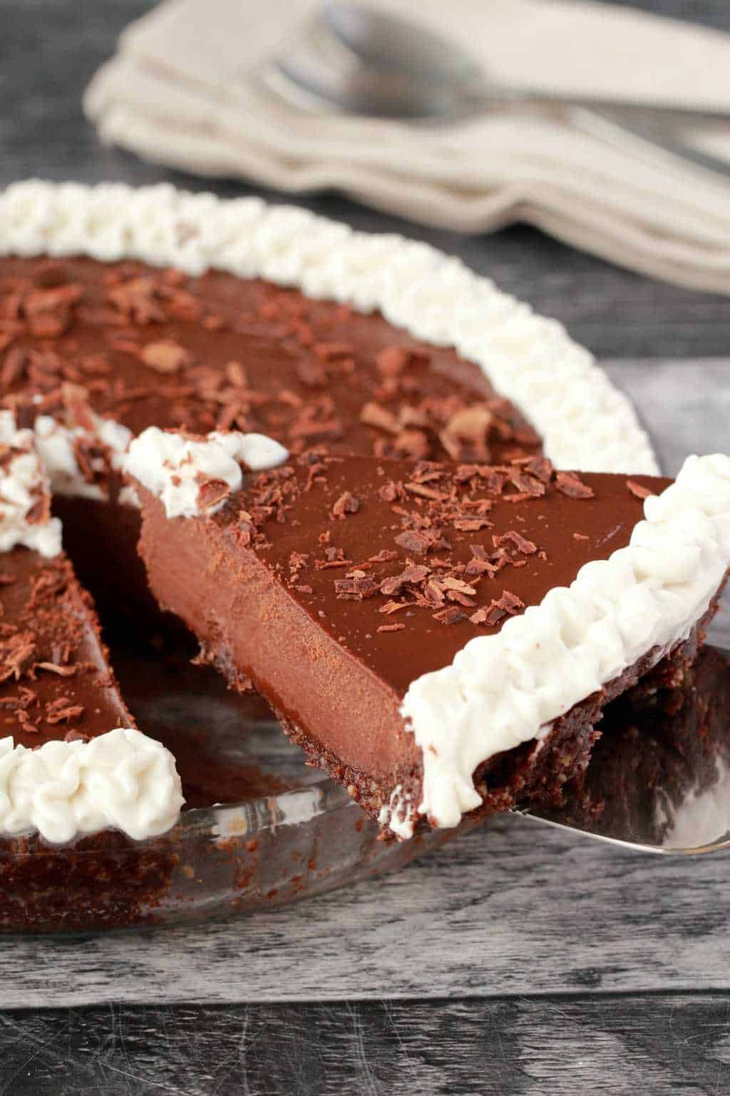 Tarte au chocolat végétalienne décorée de crème de noix de coco fouettée et de flocons de chocolat dans un plat à tarte en verre. 