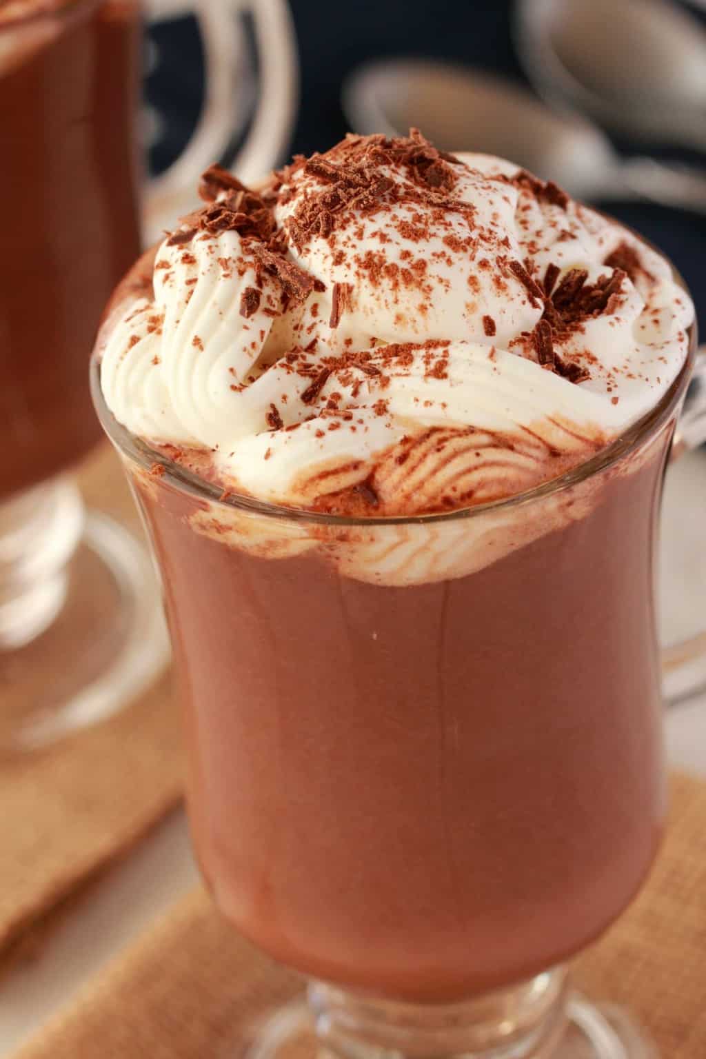 Chocolat chaud végétalien dans une tasse en verre garnie de crème fouettée et de copeaux de chocolat.