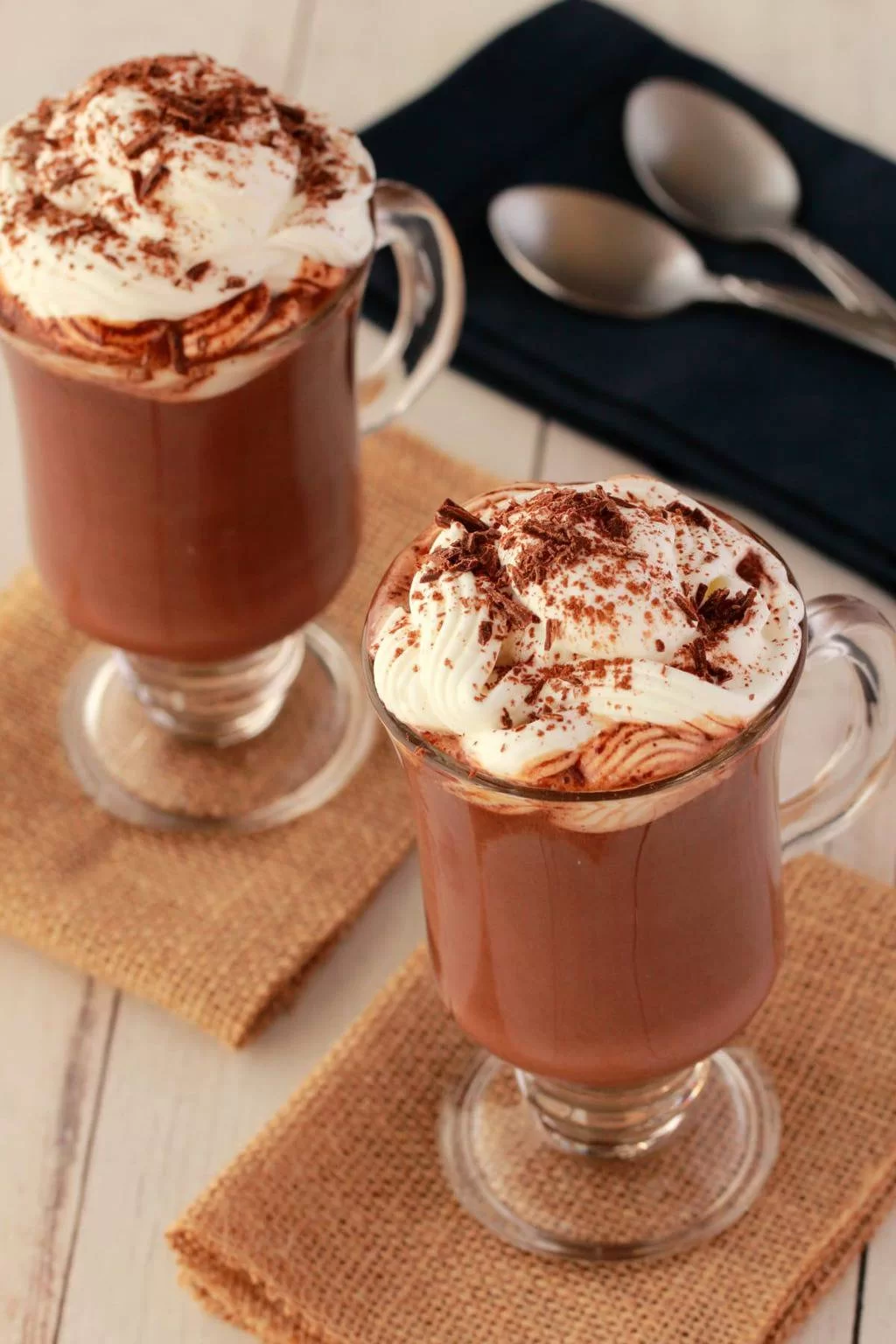 Chocolat chaud végétalien dans des tasses en verre, avec une serviette et des cuillères en arrière-plan.