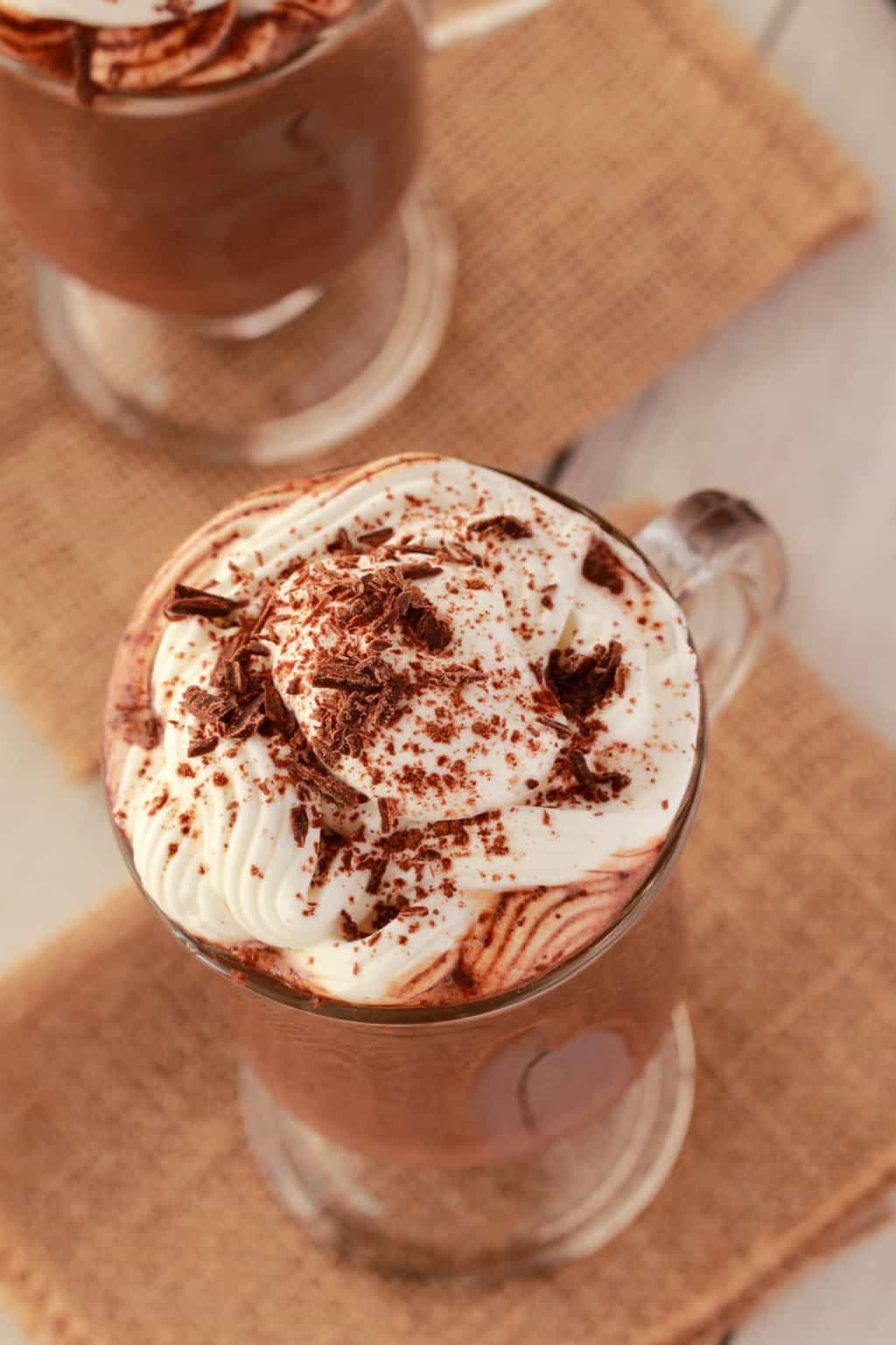 Chocolat chaud végétalien dans des tasses en verre avec de la crème fouettée et des copeaux de chocolat sur le dessus. 