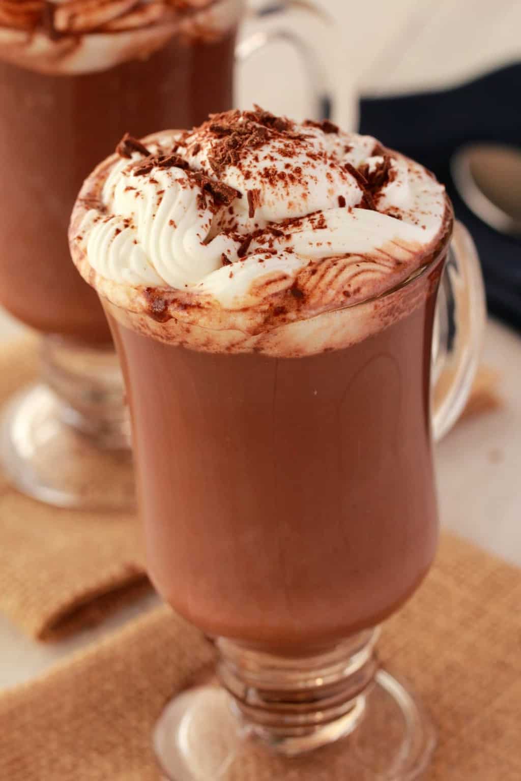 Chocolat chaud végétalien dans une tasse en verre garnie de crème fouettée végétalienne et de copeaux de chocolat. 