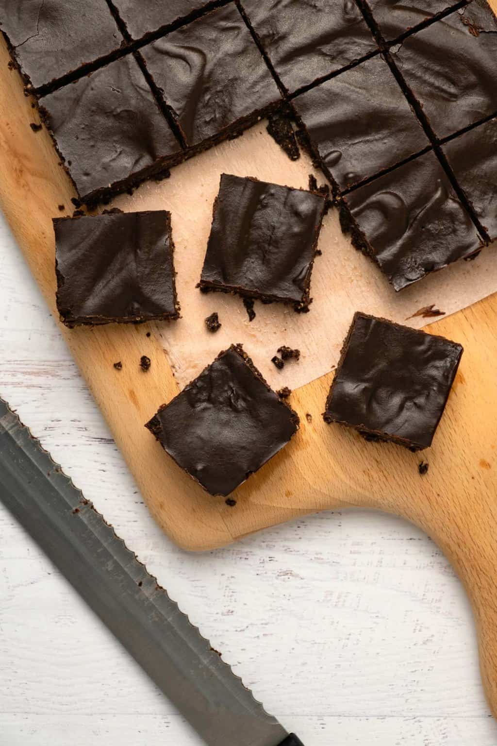 Brownies végétaliens crus coupés en carrés sur une planche à découper en bois.