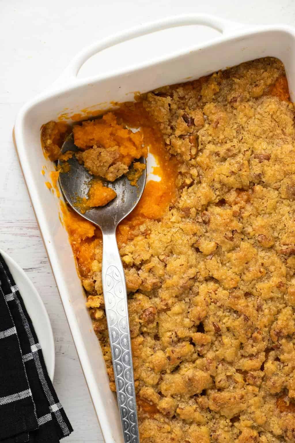Casserole de patates douces végétaliennes dans un plat blanc avec une cuillère de service.