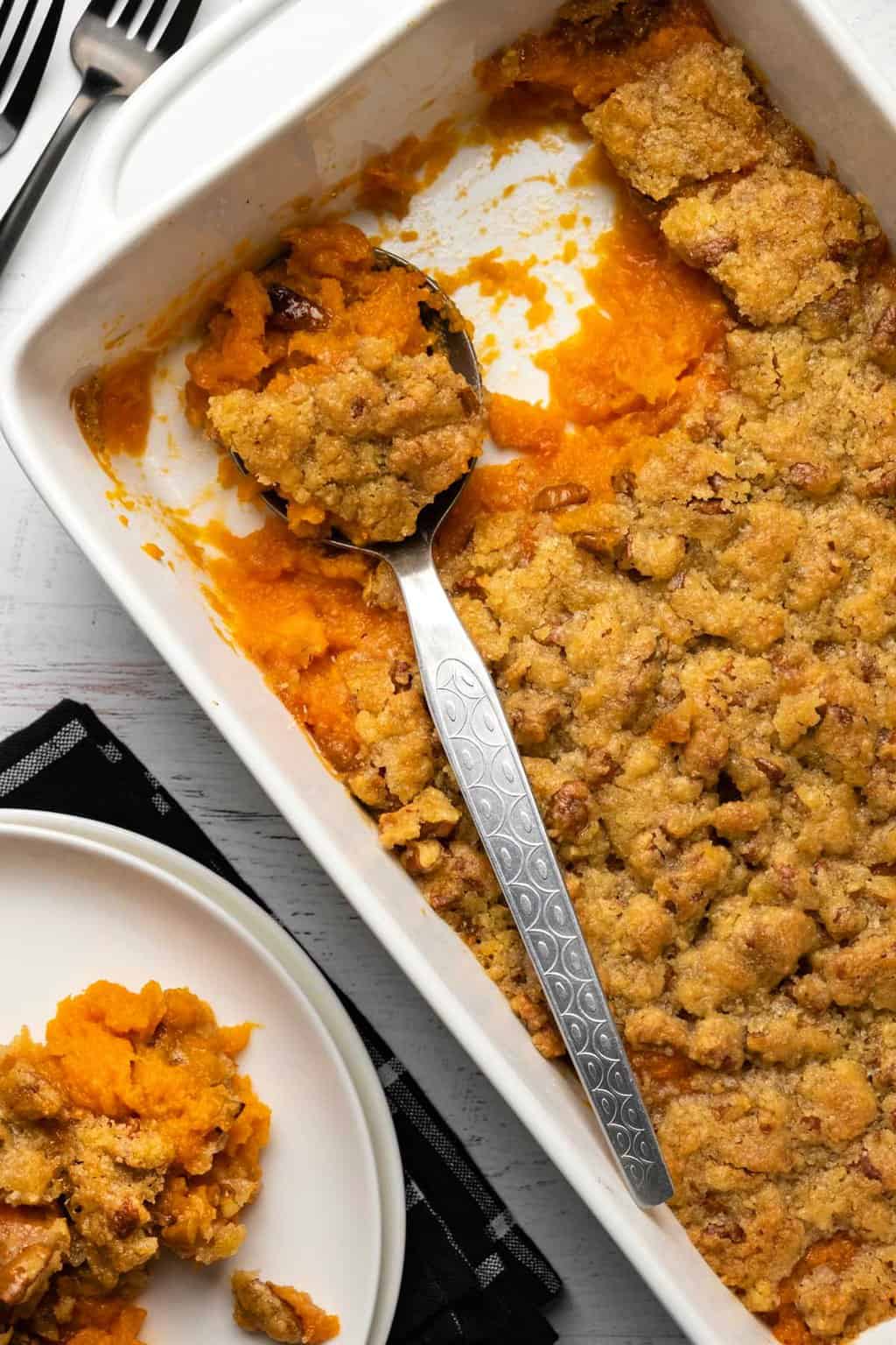 Casserole végétalienne de patates douces dans un plat blanc avec une cuillère de service en argent.