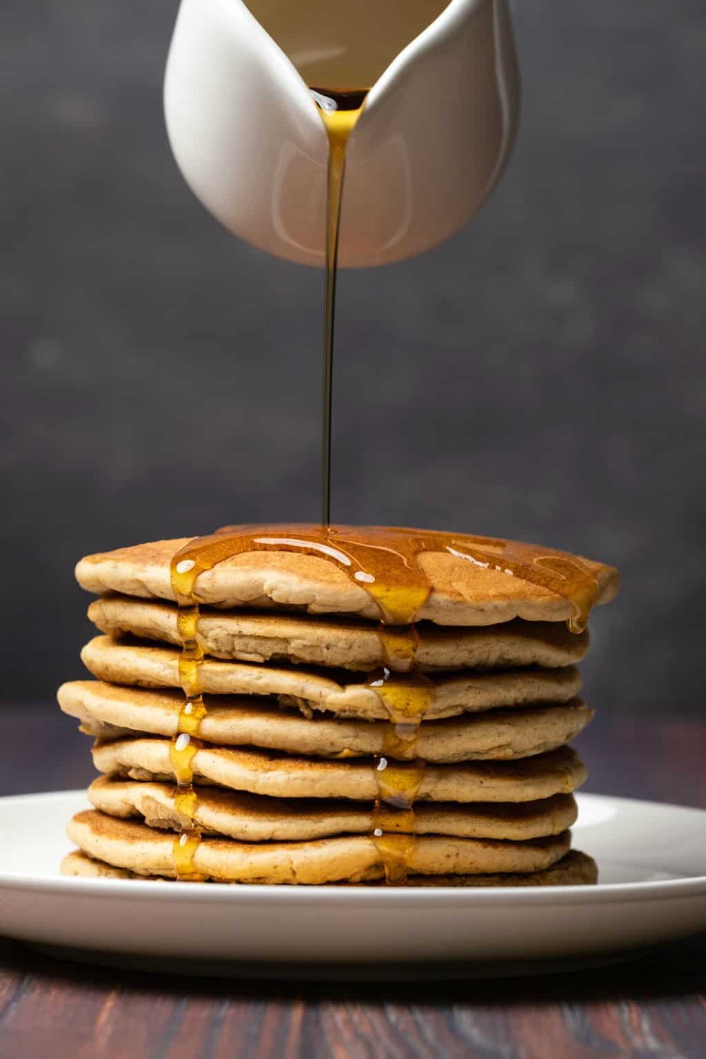 Une pile de crêpes protéinées végétaliennes avec du sirop coulant sur le dessus.