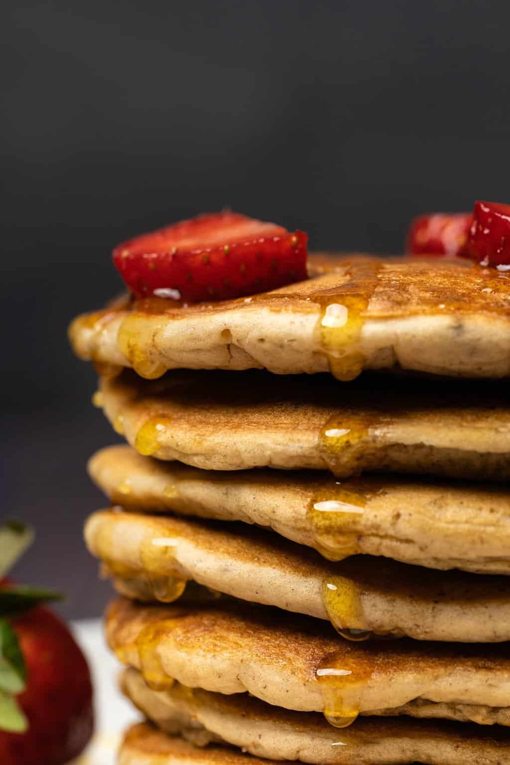 Une pile de crêpes garnie de fraises et arrosée de sirop.