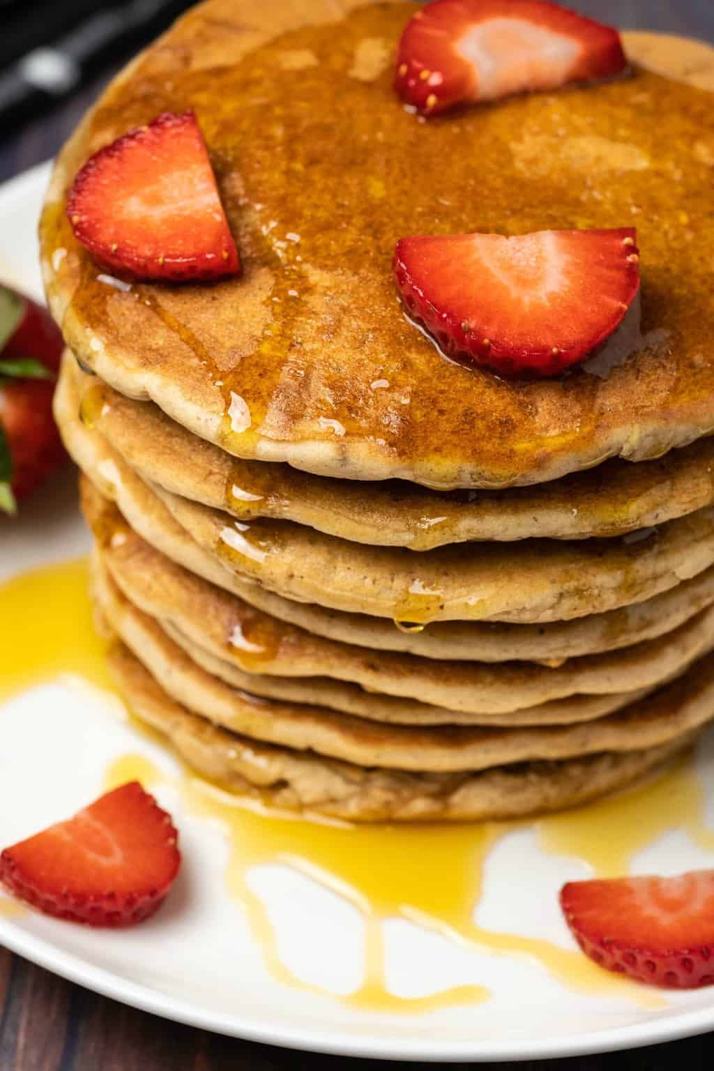 Une pile de crêpes végétaliennes garnie de fraises fraîches et de sirop.