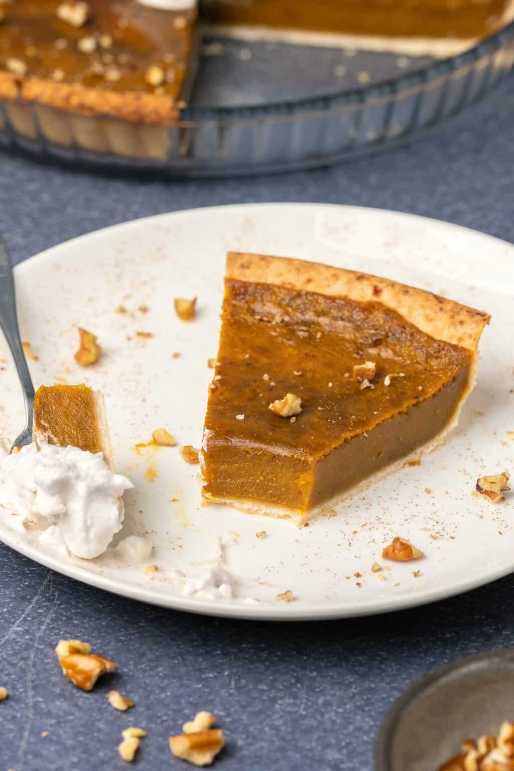 Une tranche de tarte aux patates douces végétaliennes sur une plaque blanche avec une fourchette à gâteau.