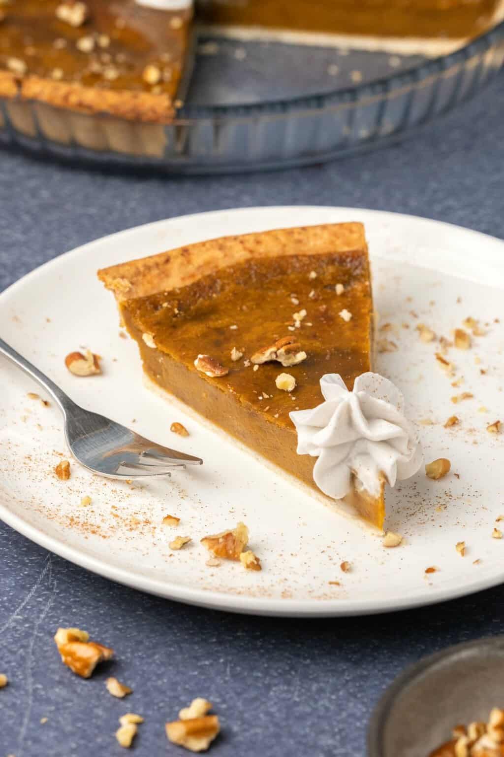 Une tranche de tarte aux patates douces végétaliennes sur une plaque blanche avec une fourchette à gâteau.