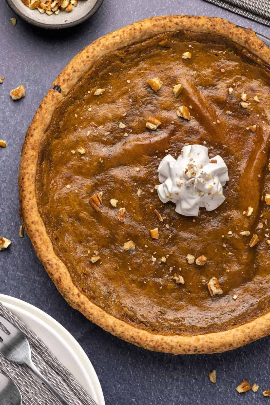 Tarte aux patates douces végétalienne garnie de pacanes hachées et de crème fouettée végétalienne.