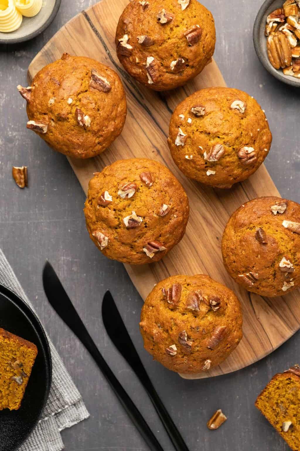 Muffins citrouilles végétaliens garnis de pacanes hachées sur une planche de bois.