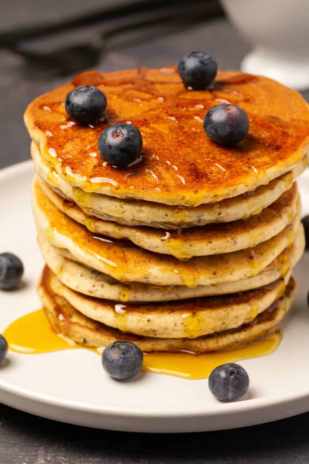 Crêpes végétaliennes sans gluten dans une pile garnie de sirop et de bleuets frais. 