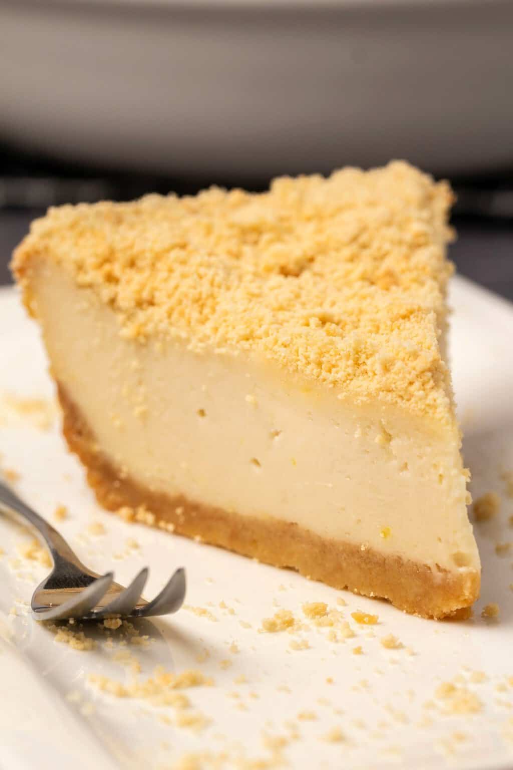 Tranche de gâteau au fromage sans produits laitiers sur une plaque blanche avec une fourchette à gâteau.