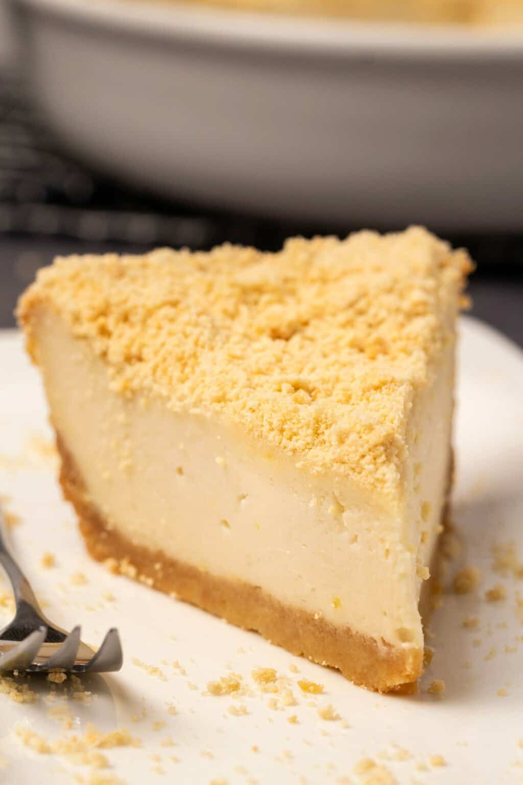 Tranche de gâteau au fromage végétalien sur une plaque blanche avec une fourchette à gâteau.