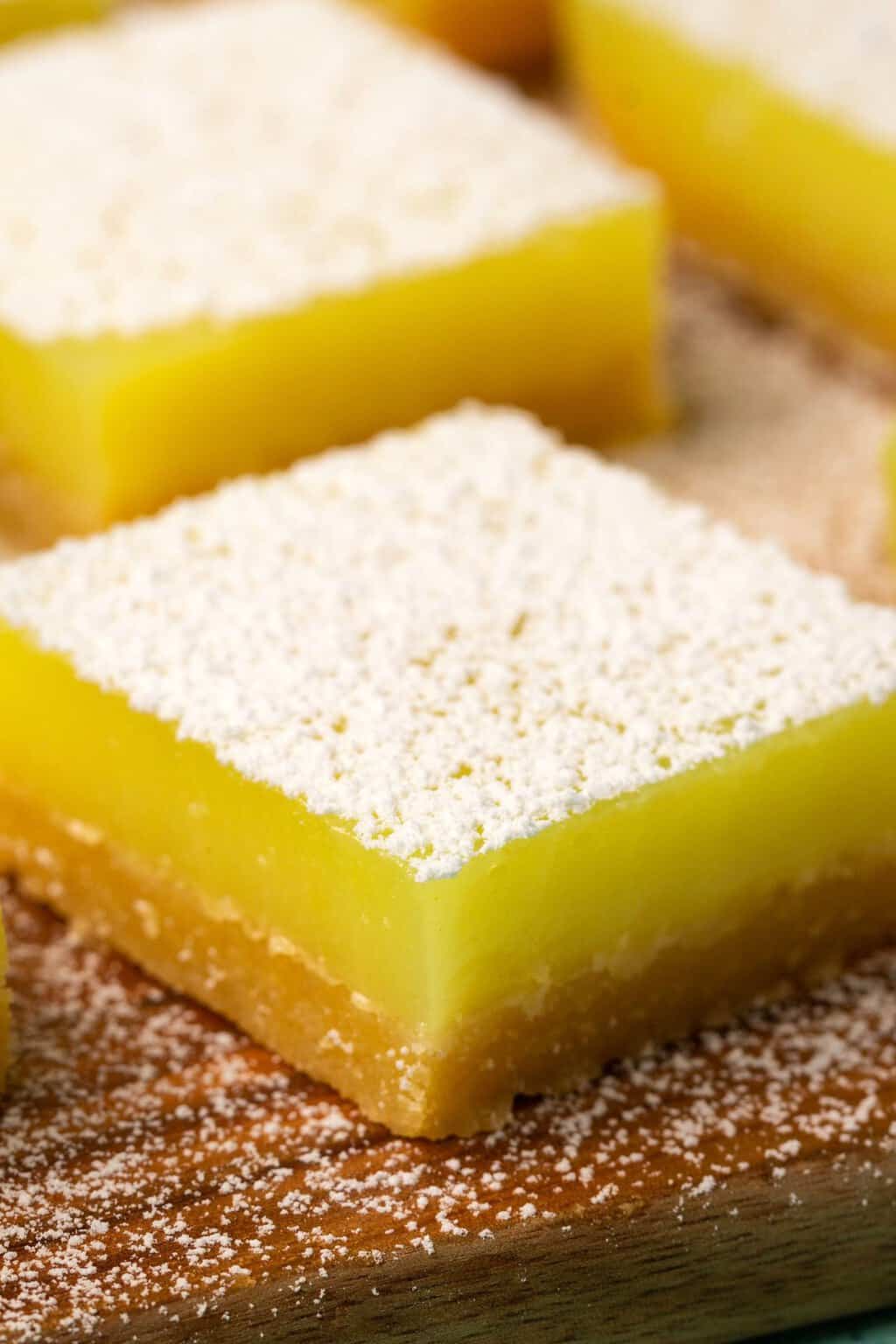 Barres de citron végétaliennes garnies de sucre en poudre sur une planche de bois.