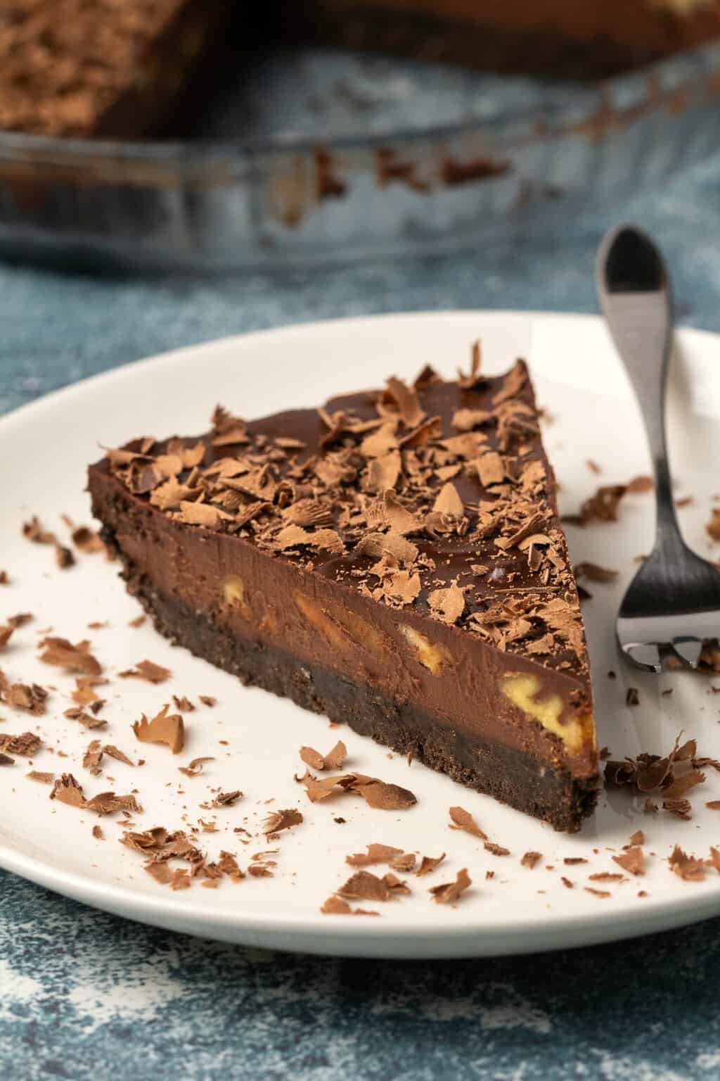 Tranche de tarte au chocolat végétalien sur une plaque blanche avec une fourchette à gâteau.