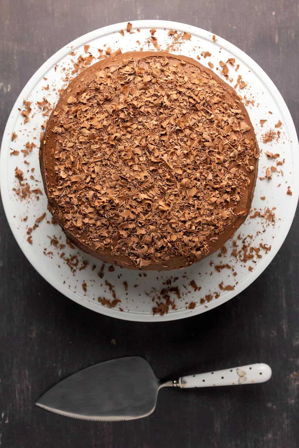 Gâteau au chocolat sans produits laitiers avec glaçage au chocolat au beurre végétalien sur un stand de gâteau blanc.