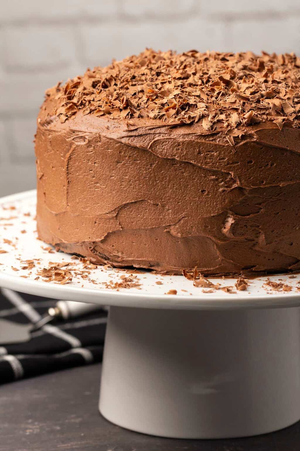 Crème au beurre au chocolat végétalien glaçage sur un gâteau au chocolat sur un stand de gâteau blanc.