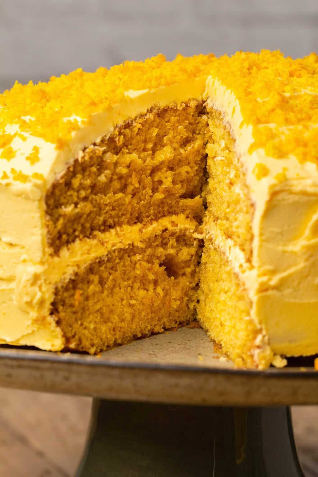 Gâteau orange végétalien sur un stand de gâteau avec une tranche manquante. 