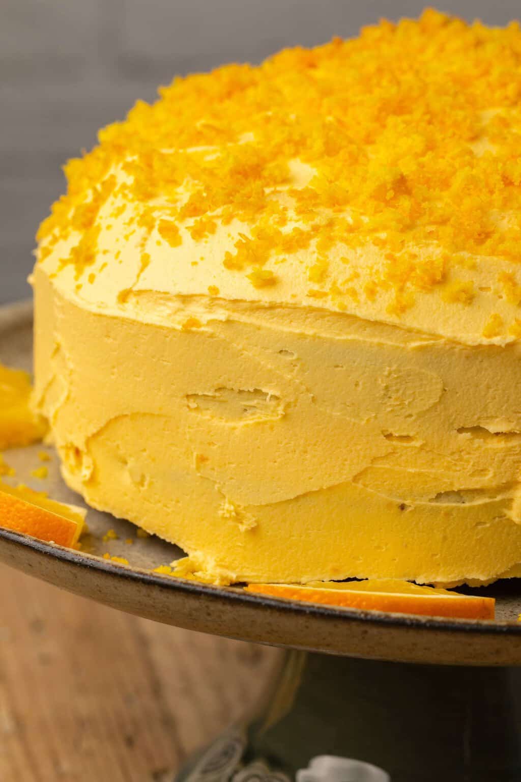 Gâteau orange végétalien garni de zeste d'orange sur un support à gâteau. 