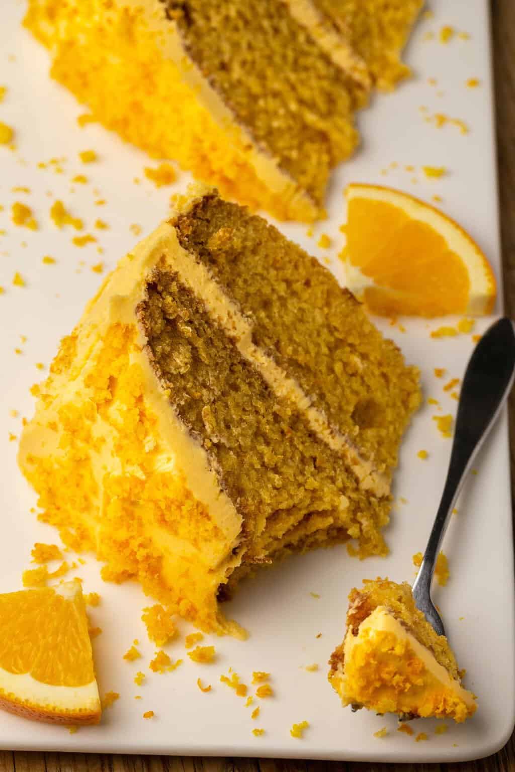 Tranche de gâteau orange végétalien sur une plaque blanche avec une fourchette à gâteau. 