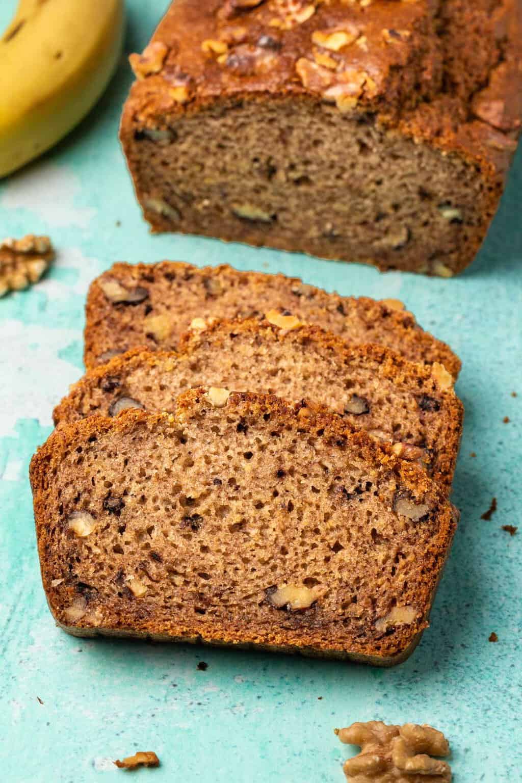 Une miche de pain aux bananes sans gluten végétalien avec 3 tranches coupées devant.