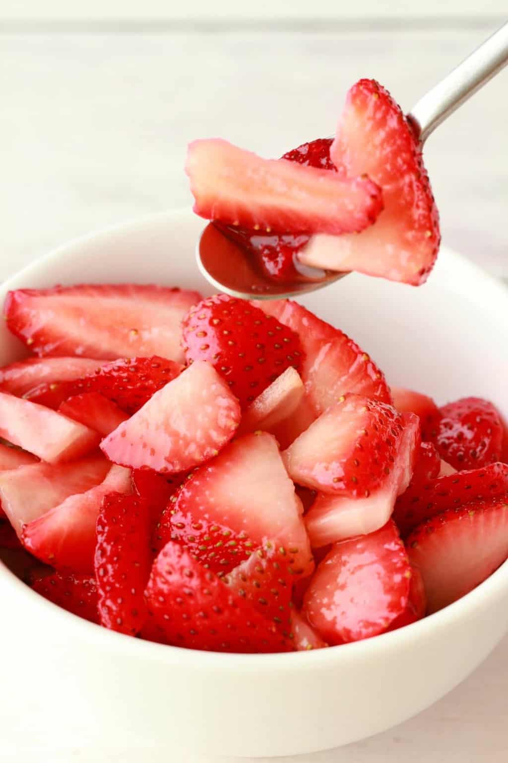 Fraises tranchées dans un bol blanc avec une cuillère. 