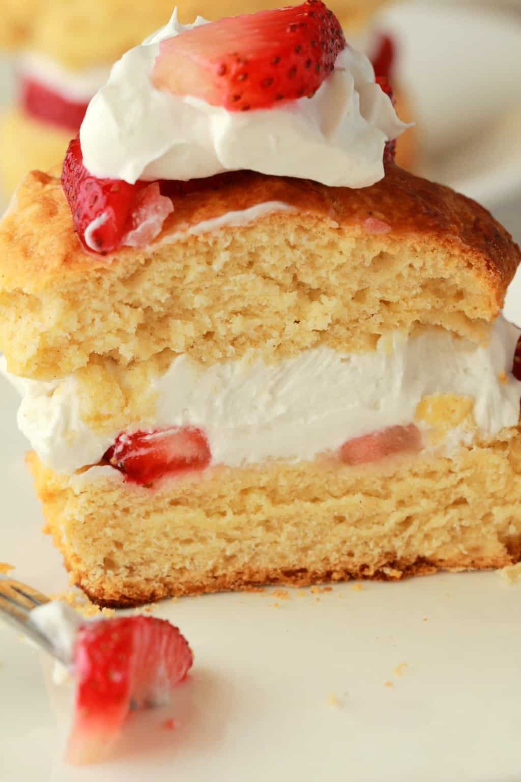 Sablé aux fraises végétalien garni de crème fouettée végétalienne et de fraises fraîches coupées en deux sur une plaque blanche. 