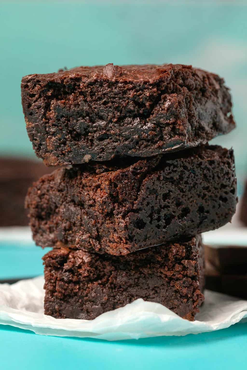 Brownies végétaliens sans gluten dans une pile sur du papier sulfurisé.