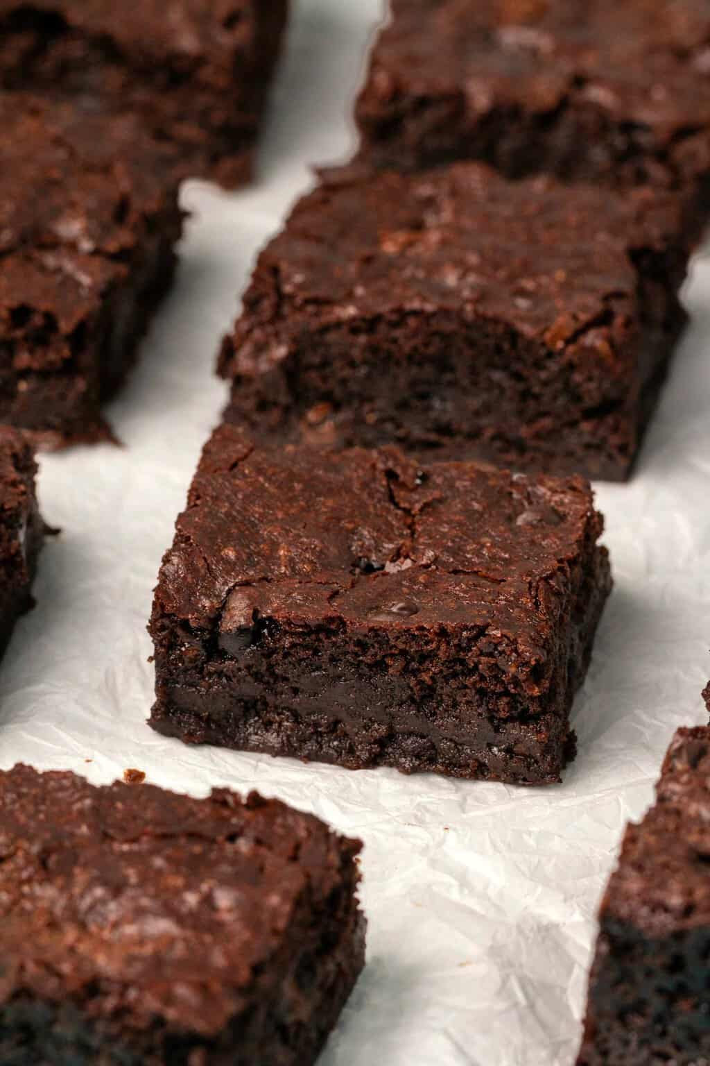 Brownies végétaliens sans gluten coupés en carrés sur du papier sulfurisé.
