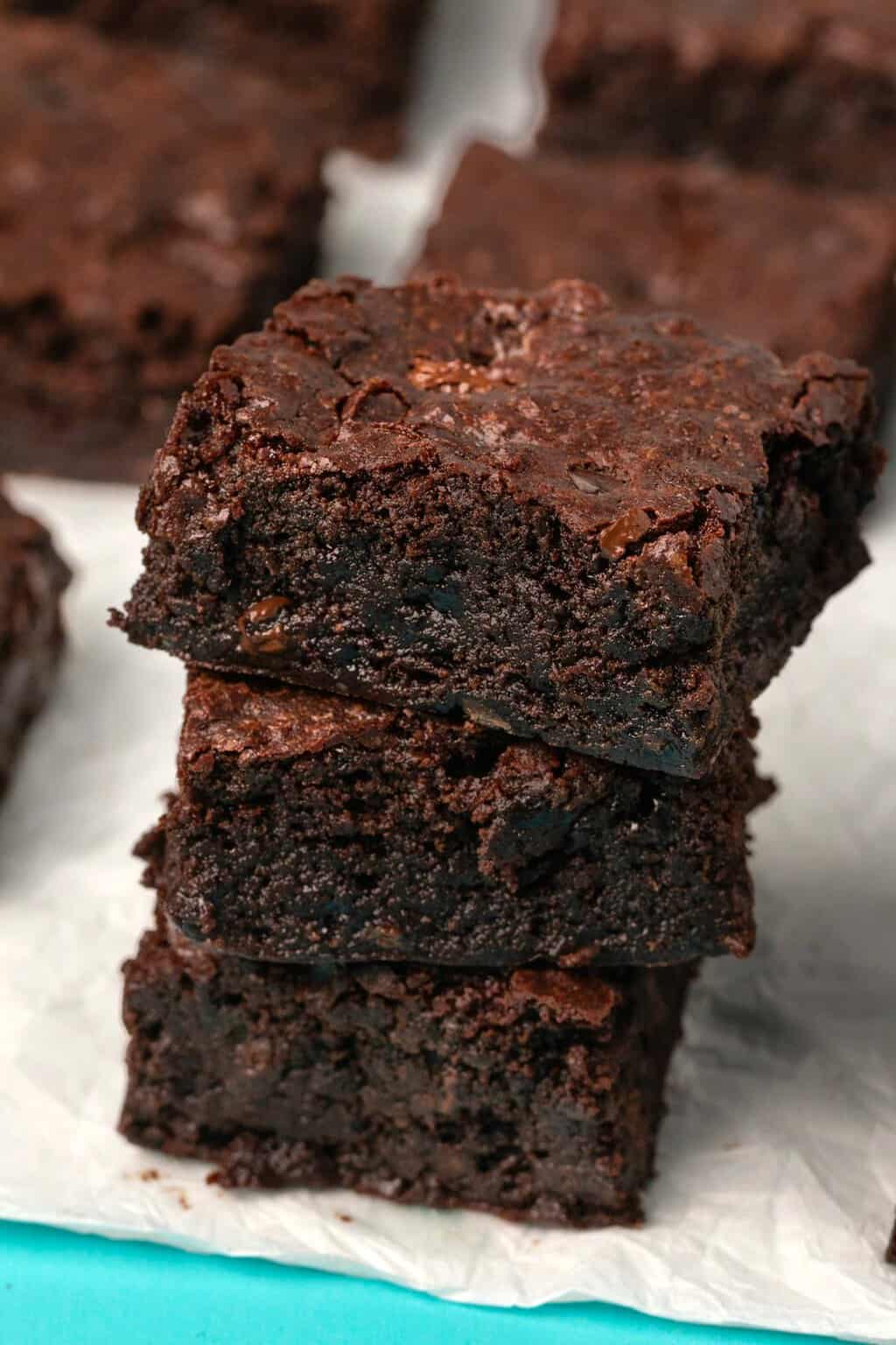 Brownies végétaliens sans gluten empilés sur du papier sulfurisé.