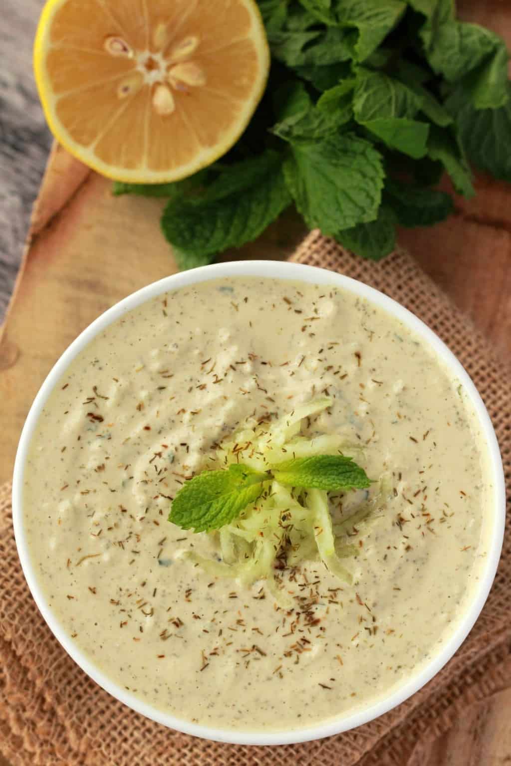 Tzatziki végétalien dans un bol blanc avec du citron frais et de la menthe en arrière-plan.