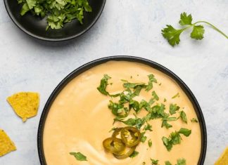 Meilleur Vegan Queso – Loving It Vegan Queso végétalien garni de piments jalapeños et de coriandre hachée dans un bol noir.