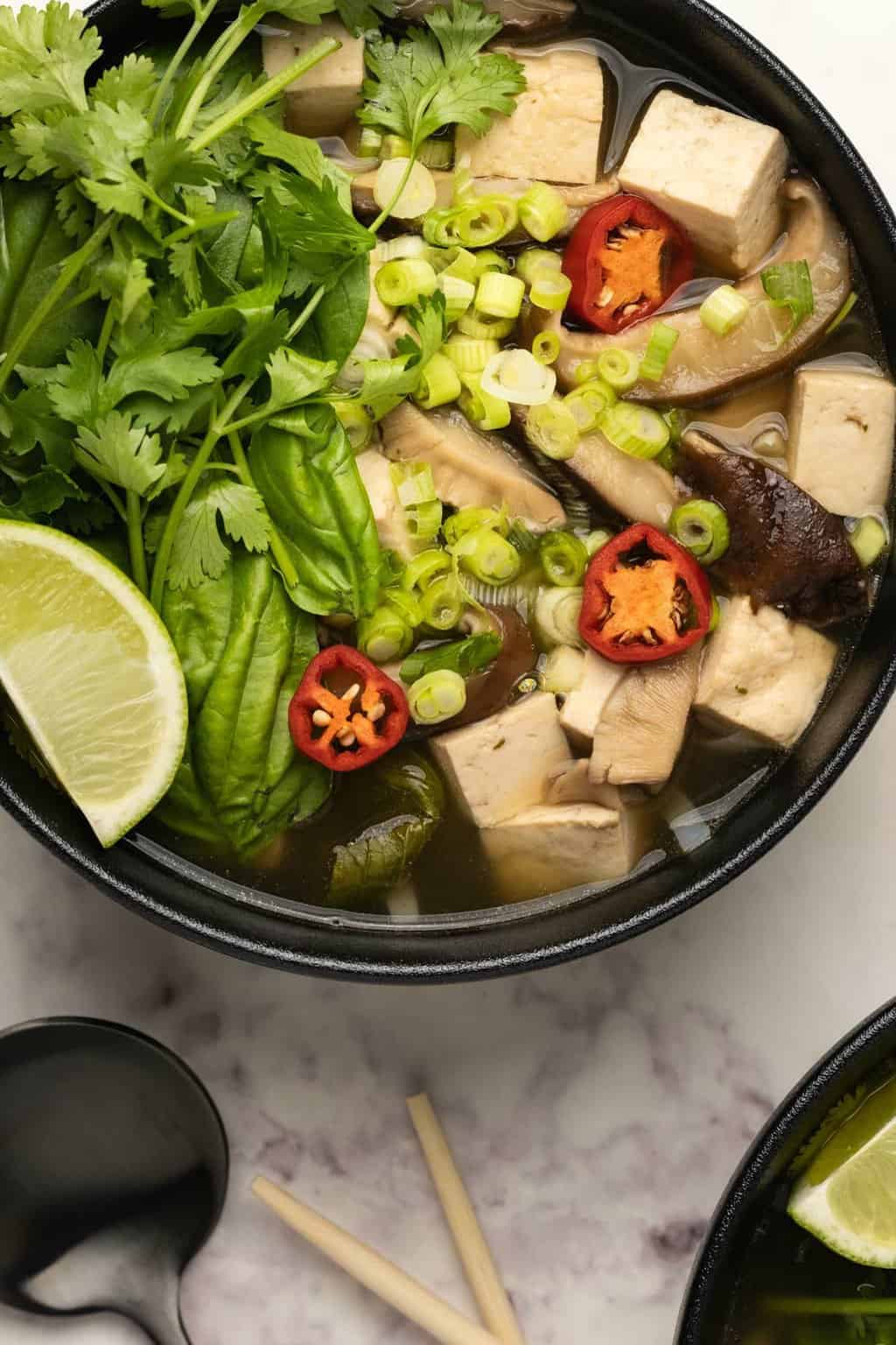 Pho végétalien aux herbes fraîches, citron vert et piment dans un bol noir. 