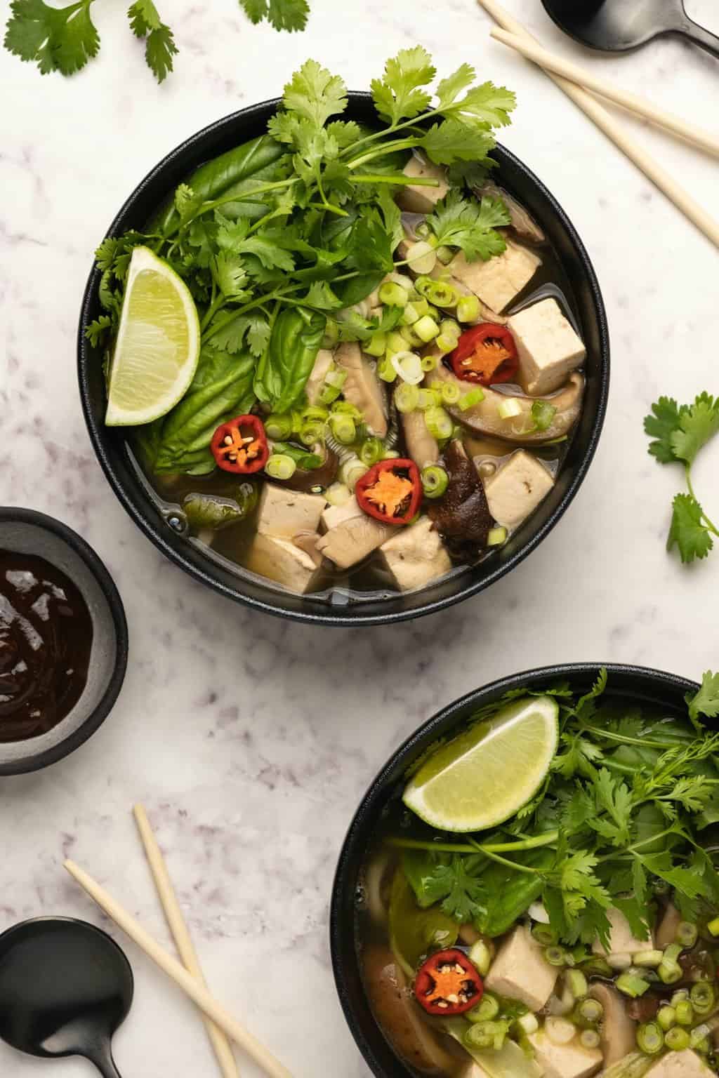 Pho végétalien garni d'herbes fraîches et de citron vert frais dans un bol noir. 