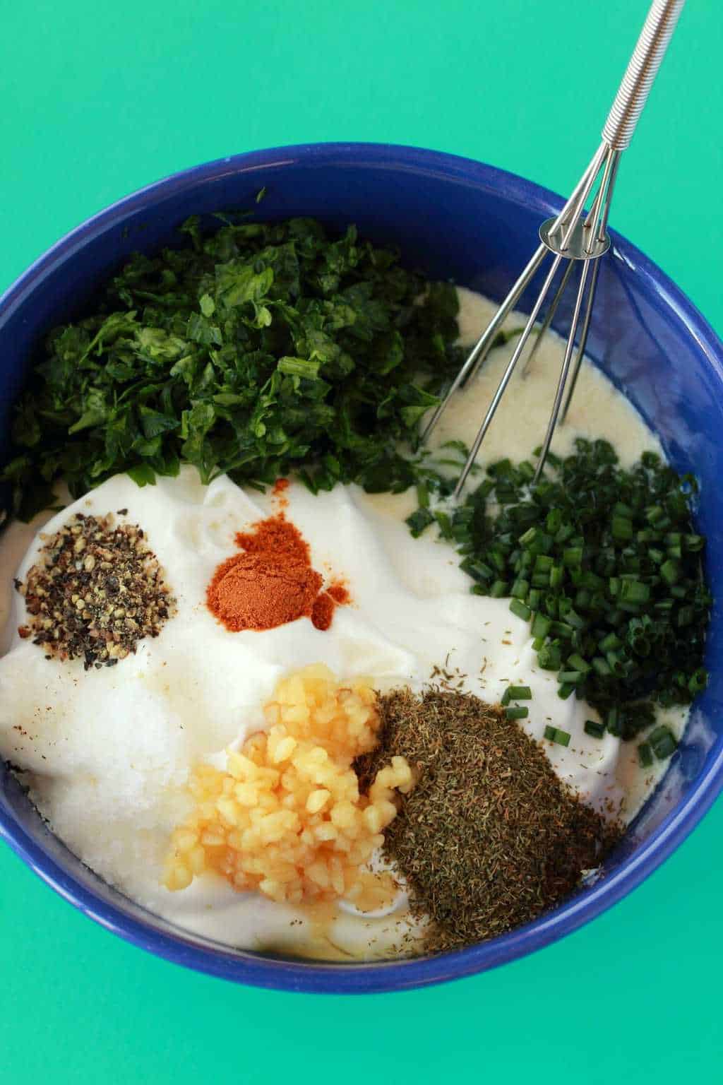 Ingrédients pour une vinaigrette ranch végétalienne dans un bol bleu avec un fouet. 