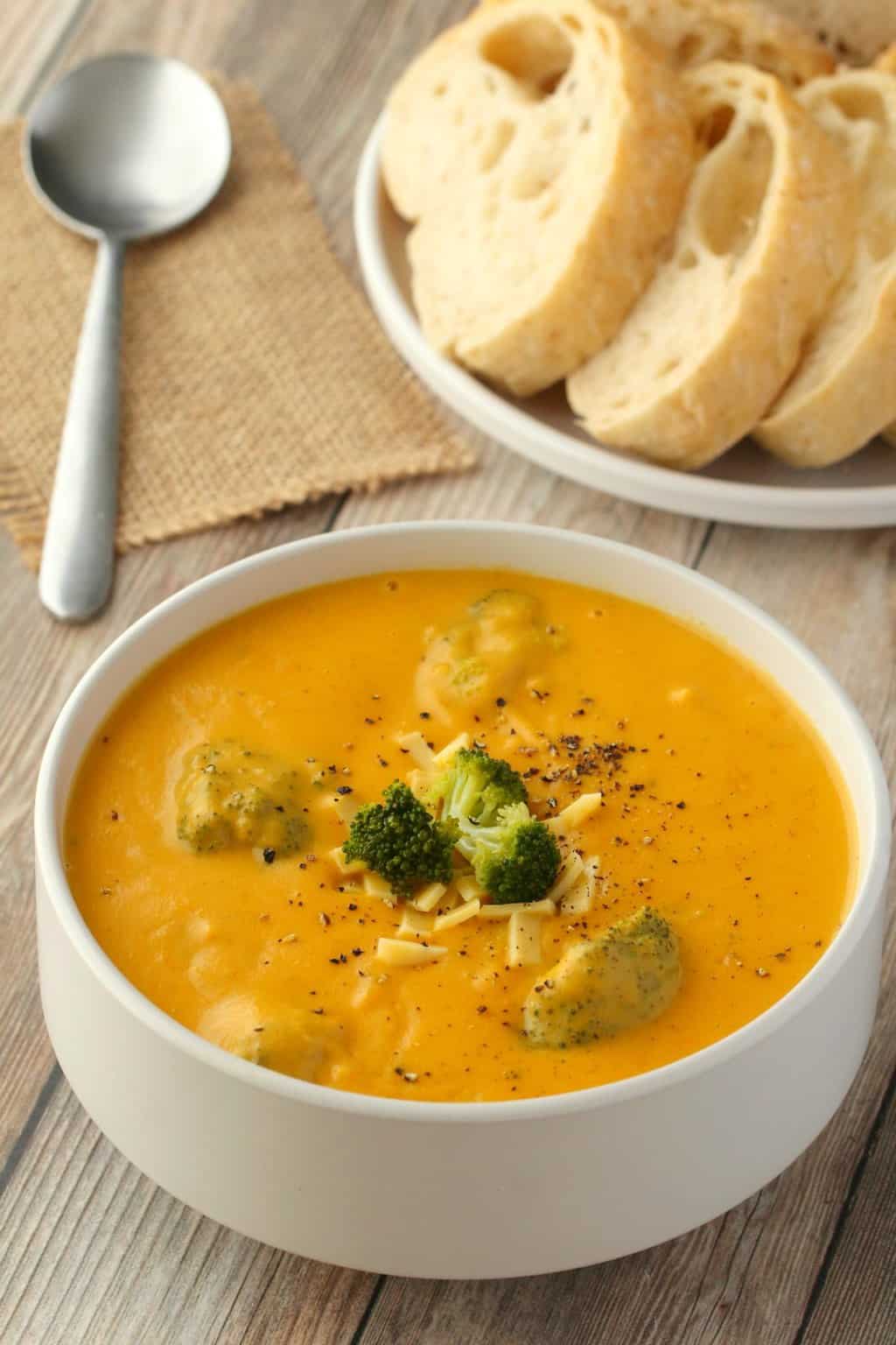 Soupe de fromage au brocoli végétalien garnie de morceaux de brocoli et de fromage végétalien râpé dans un bol blanc. 