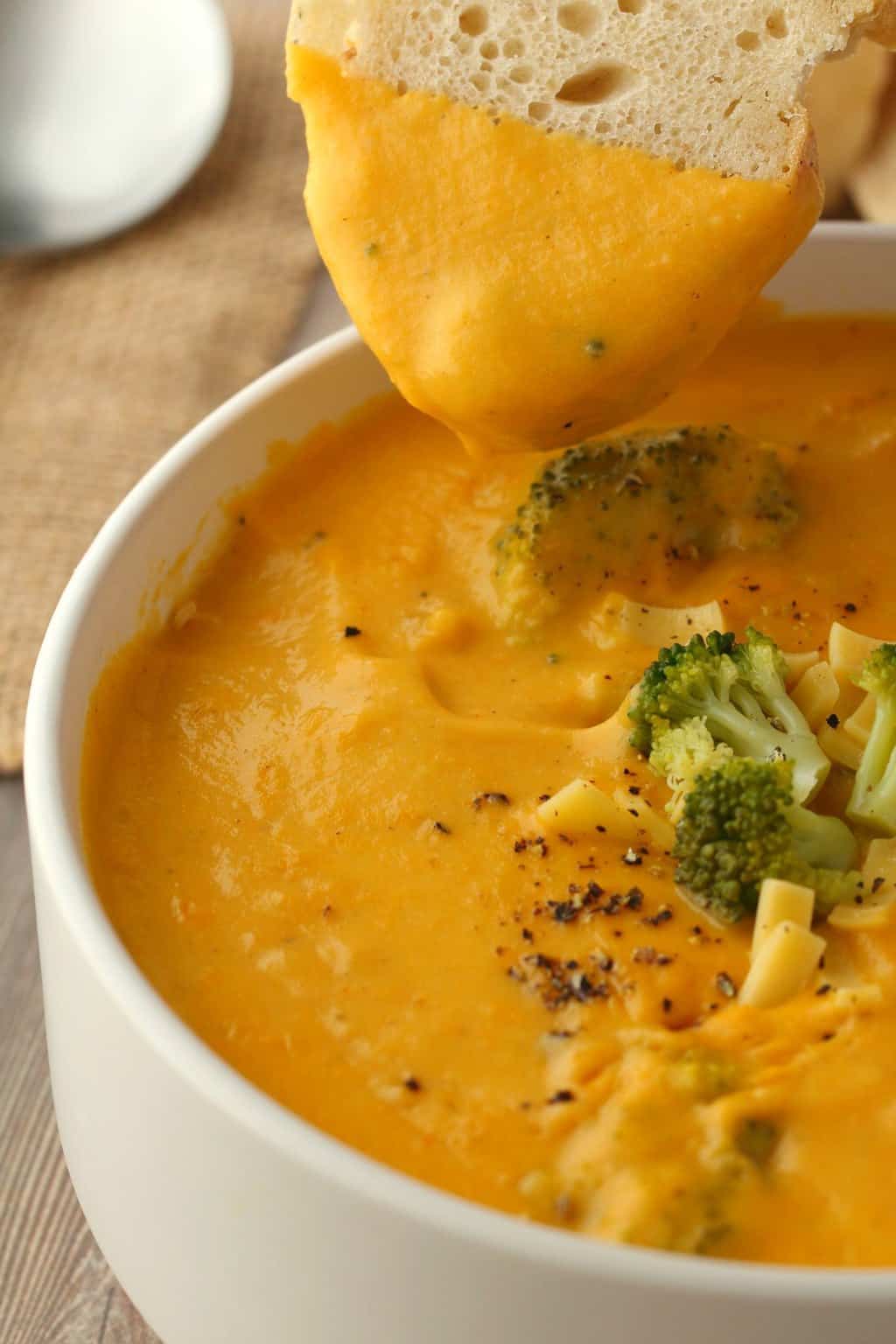 Tranche de pain plongeant dans un bol de soupe au fromage au brocoli végétalien.