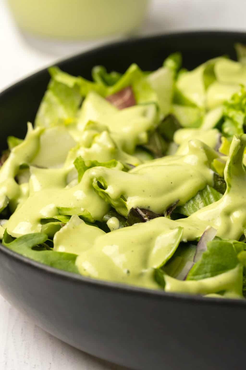 Salade verte dans un bol noir garni de vinaigrette aux noix de cajou. 
