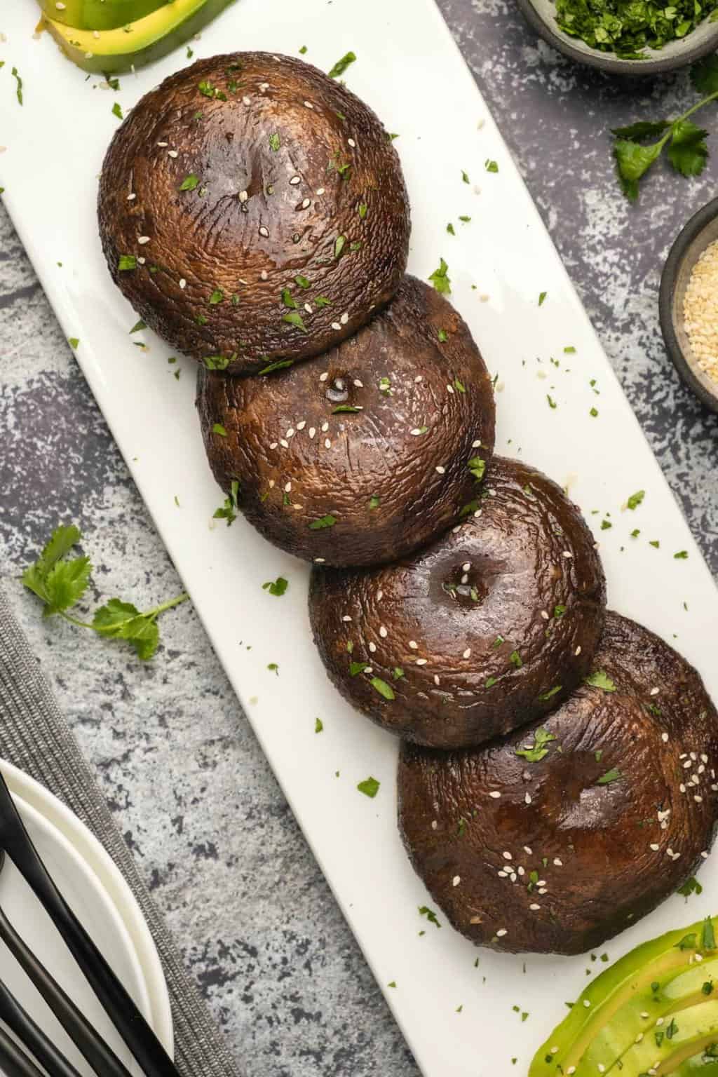 Champignons portobello au four saupoudrés de coriandre hachée et de graines de sésame sur une plaque blanche.