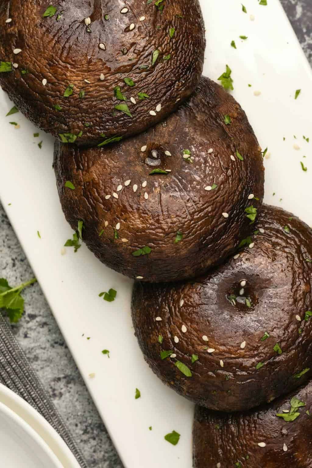 Champignons portobello au four saupoudrés de coriandre hachée et de graines de sésame sur une plaque blanche. 
