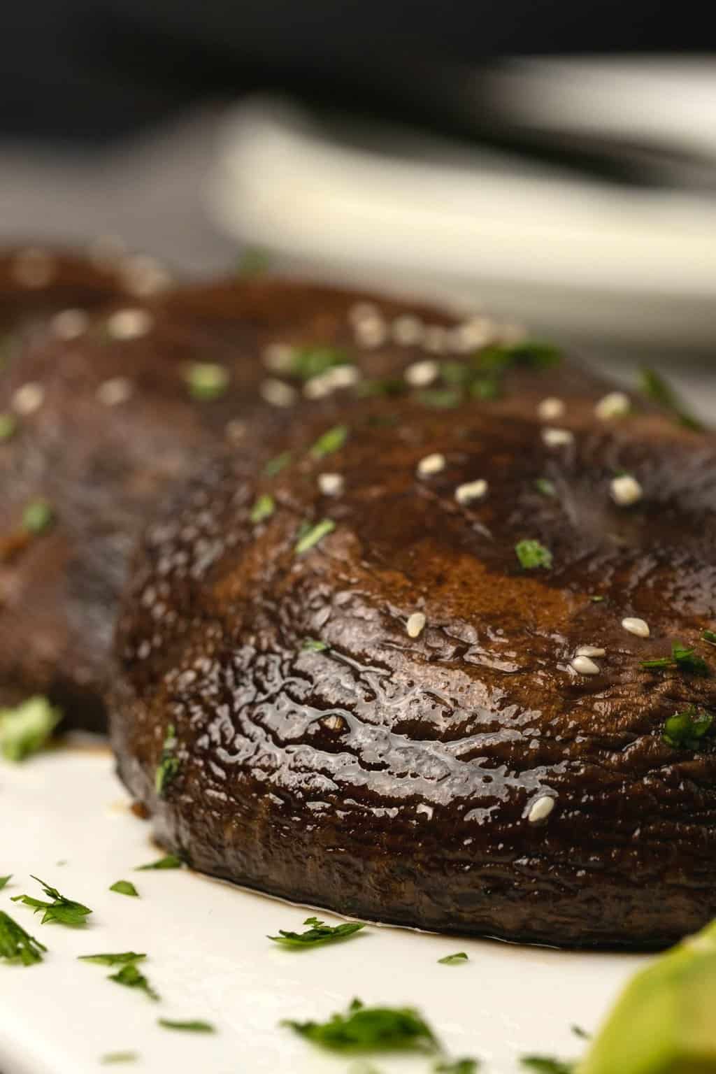 Champignons portobello au four sur une plaque blanche avec de la coriandre saupoudrée et des graines de sésame. 