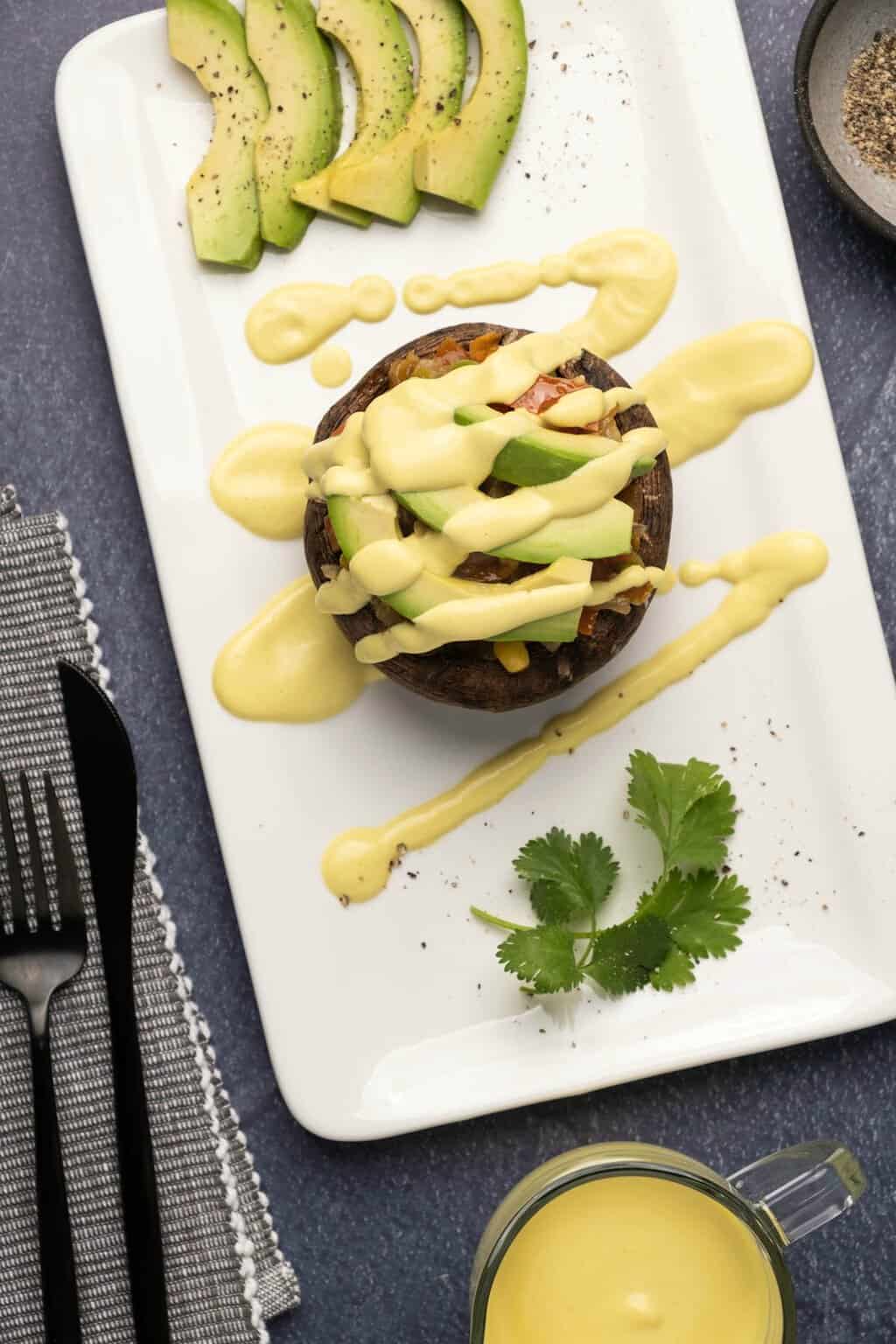 Sauce hollandaise végétalienne arrosée d'une pile de champignons rôtis et de légumes. 