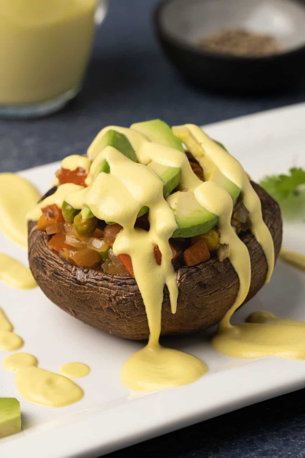 Sauce hollandaise végétalienne arrosée d'une pile de champignons rôtis et de légumes. 