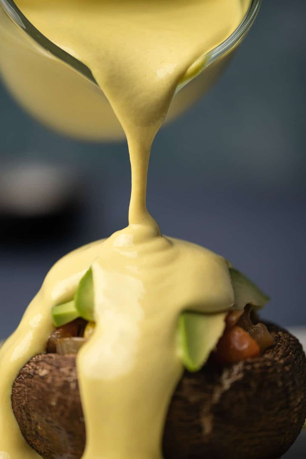 Sauce hollandaise végétalienne versée d'une cruche sur des légumes grillés. 