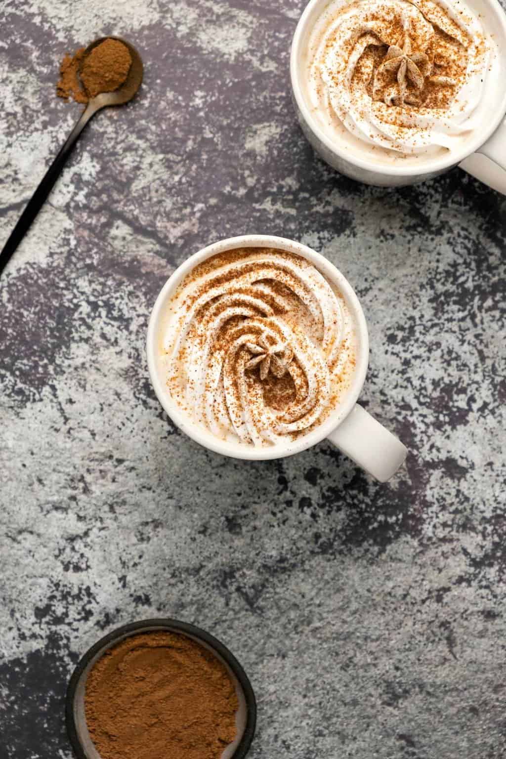Latte végétalien d'épices à la citrouille garni de crème fouettée et d'épices pour tarte à la citrouille dans une tasse blanche. 