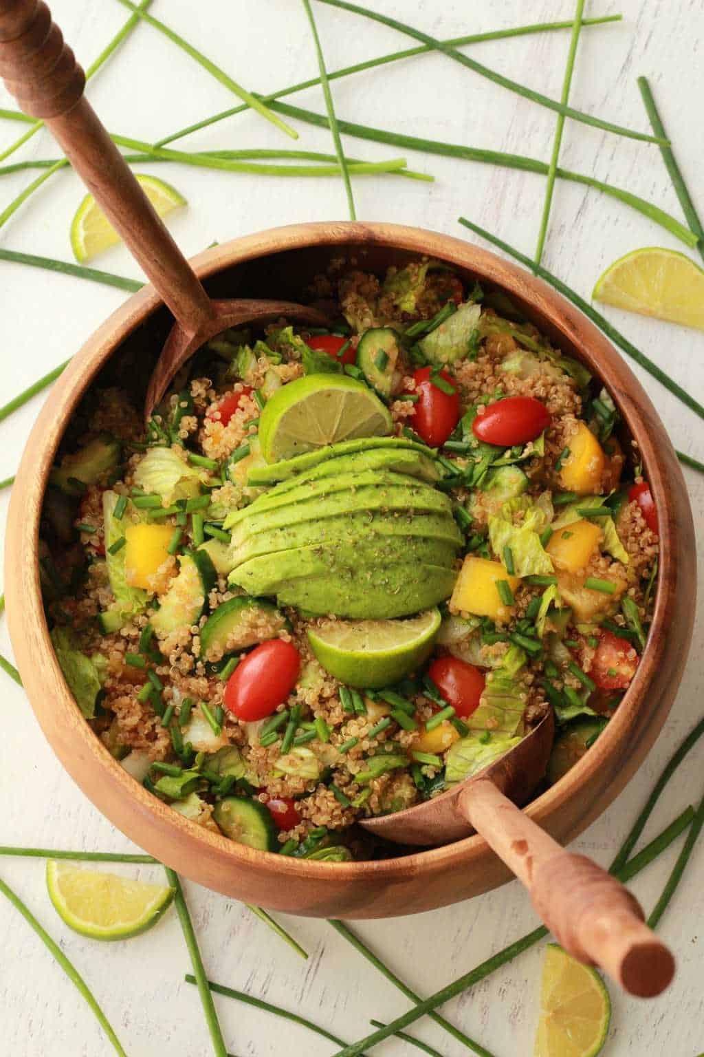 Salade de quinoa végétalienne garnie de citron vert frais et d'avocat dans un saladier en bois avec des cuillères à salade. 