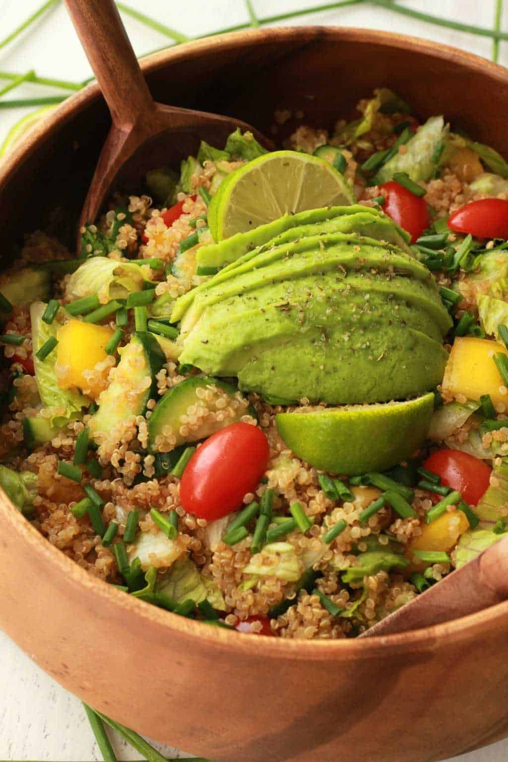 Salade de quinoa végétalienne garnie de citron vert frais et d'avocat tranché dans un saladier en bois avec des cuillères à salade. 