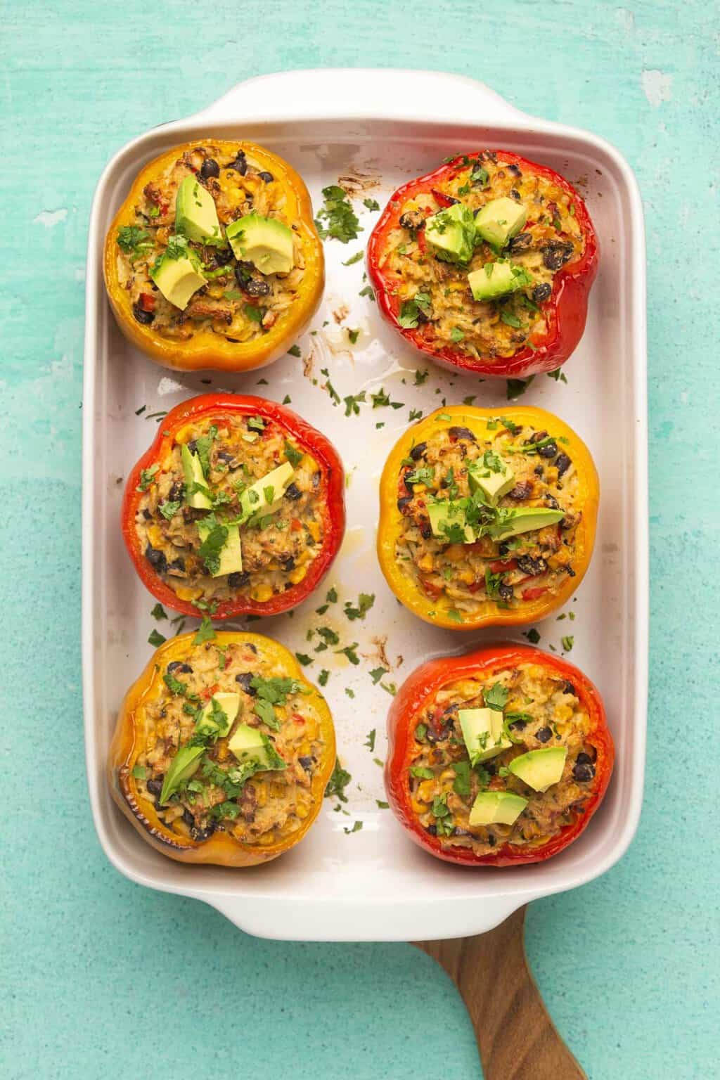 Poivrons farcis végétaliens garnis d'avocat frais et de coriandre dans un plat blanc.