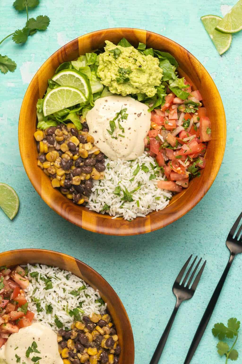 Bols à burrito végétaliens avec riz à la coriandre, haricots noirs et maïs, pico de gallo, laitue, guacamole et crème sure végétalienne.